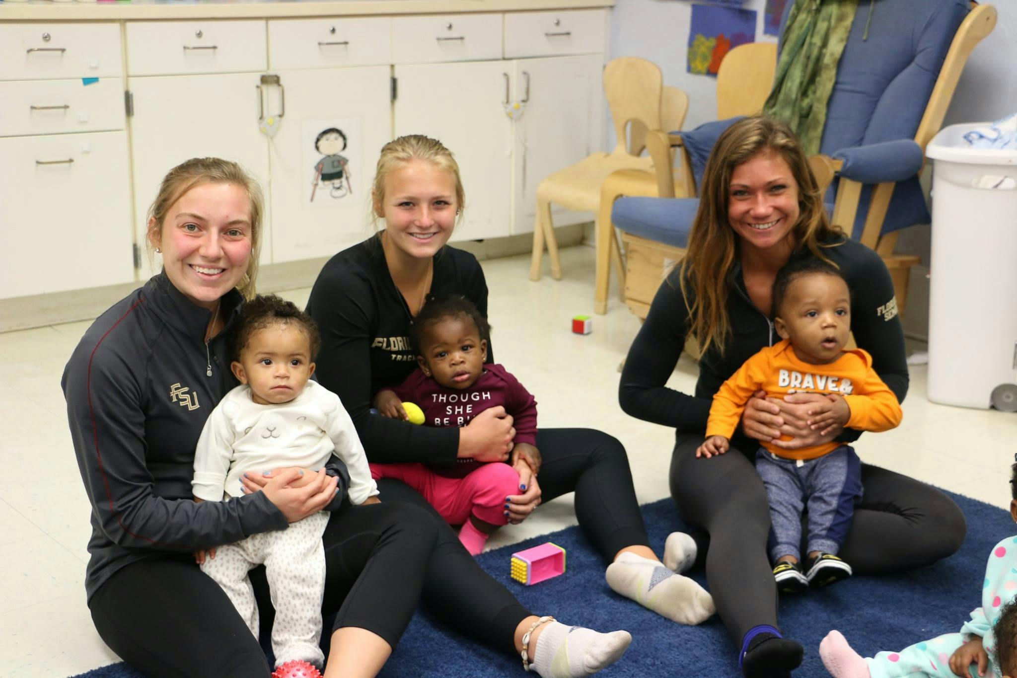 Three people sitting on a rug holding three children