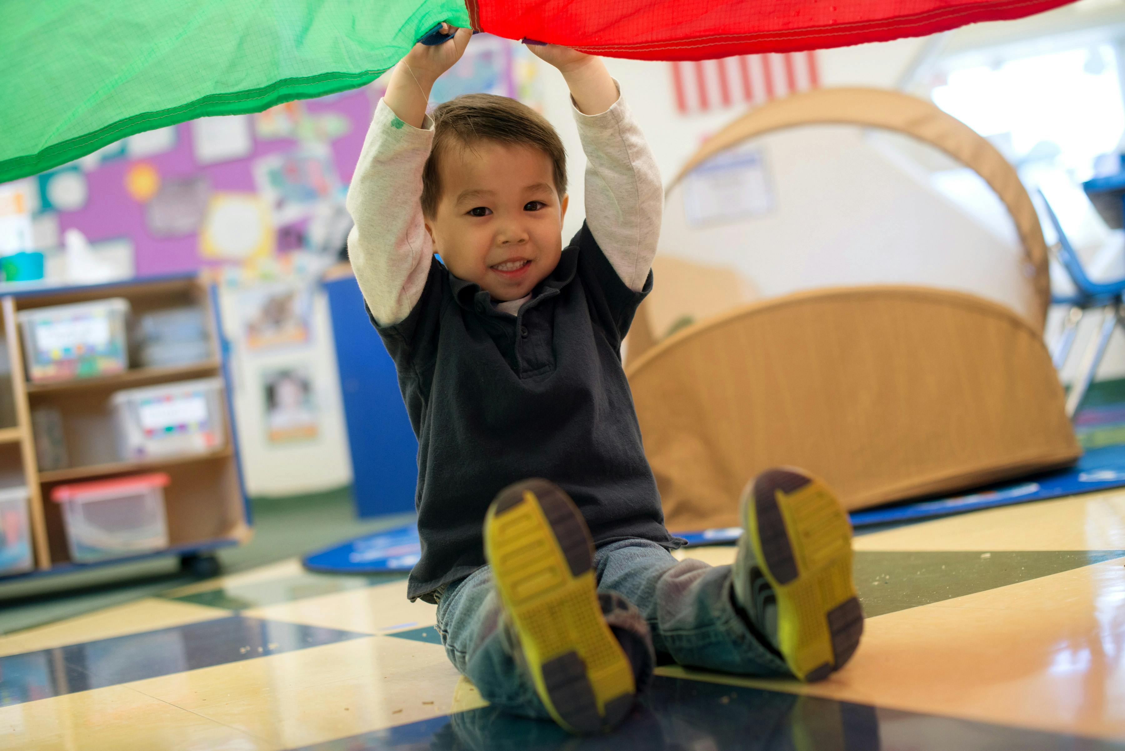 Child sitting on floor holding up a colorful parachute