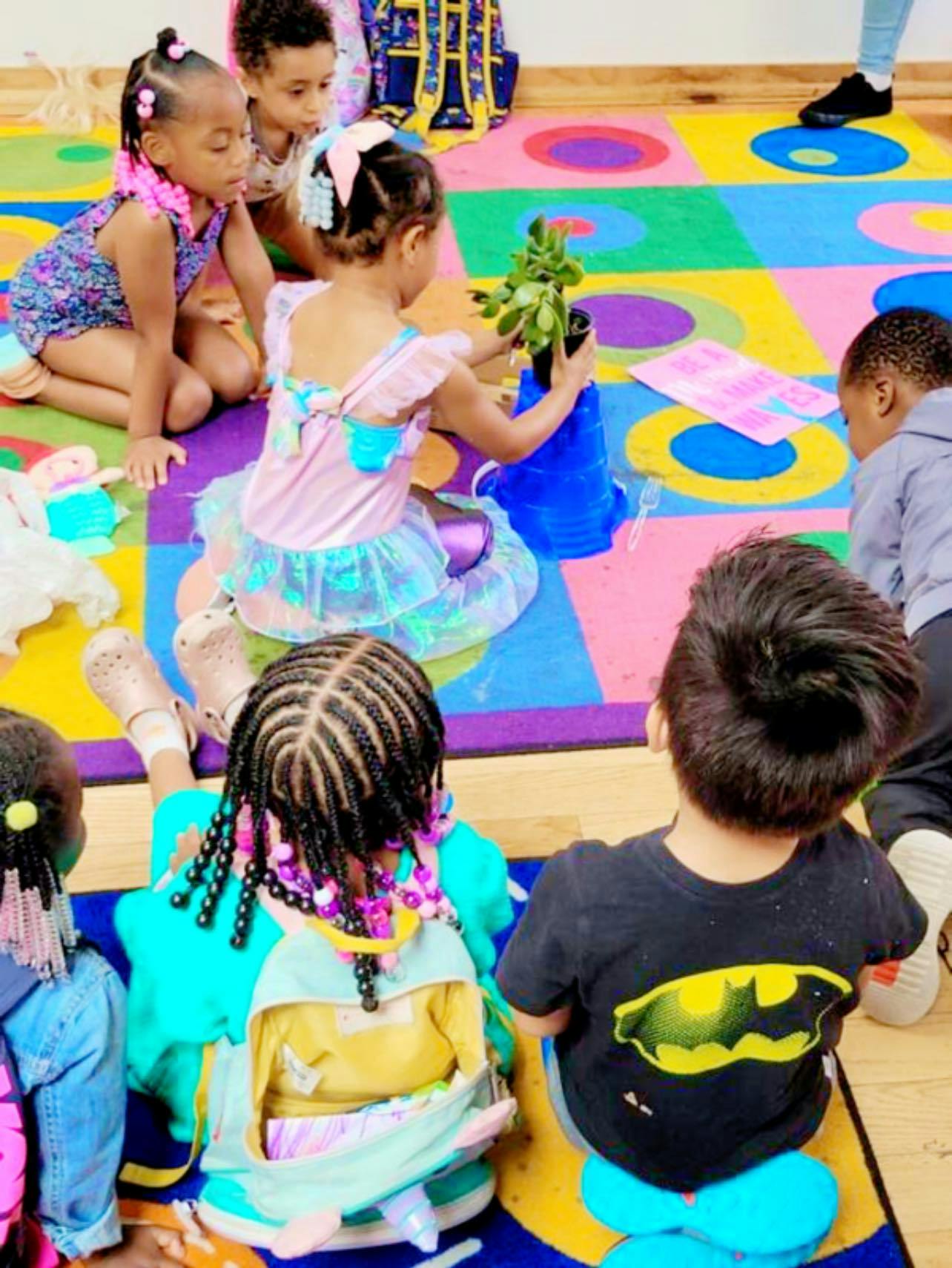 Children sitting on a colorful rug, one child holding a small plant