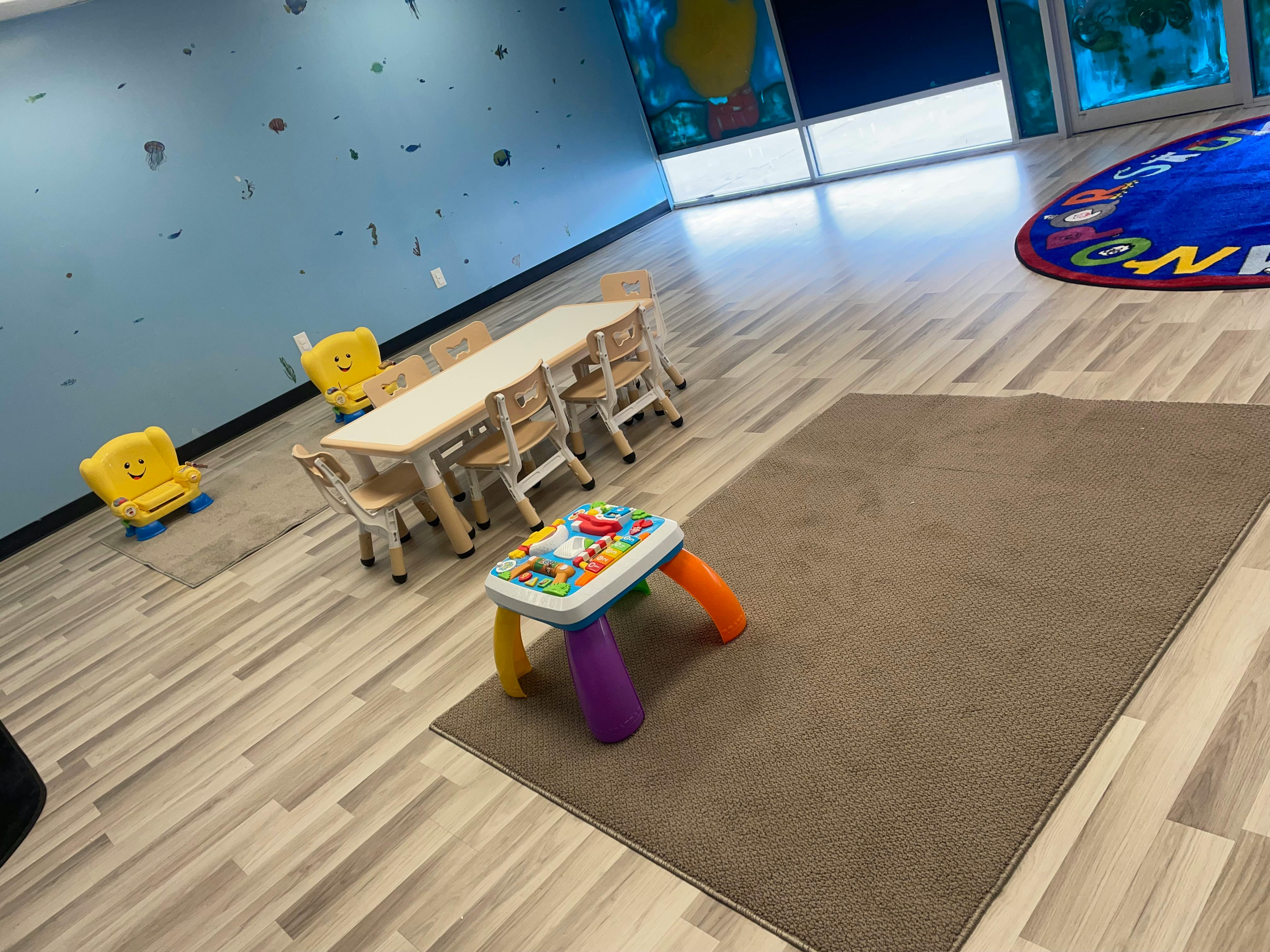 Children's play area with small table and chairs, activity toy, and rug