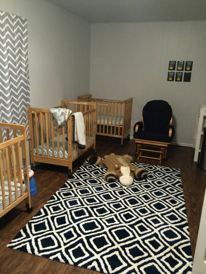 Three wooden cribs in a room with a patterned rug and a rocking chair
