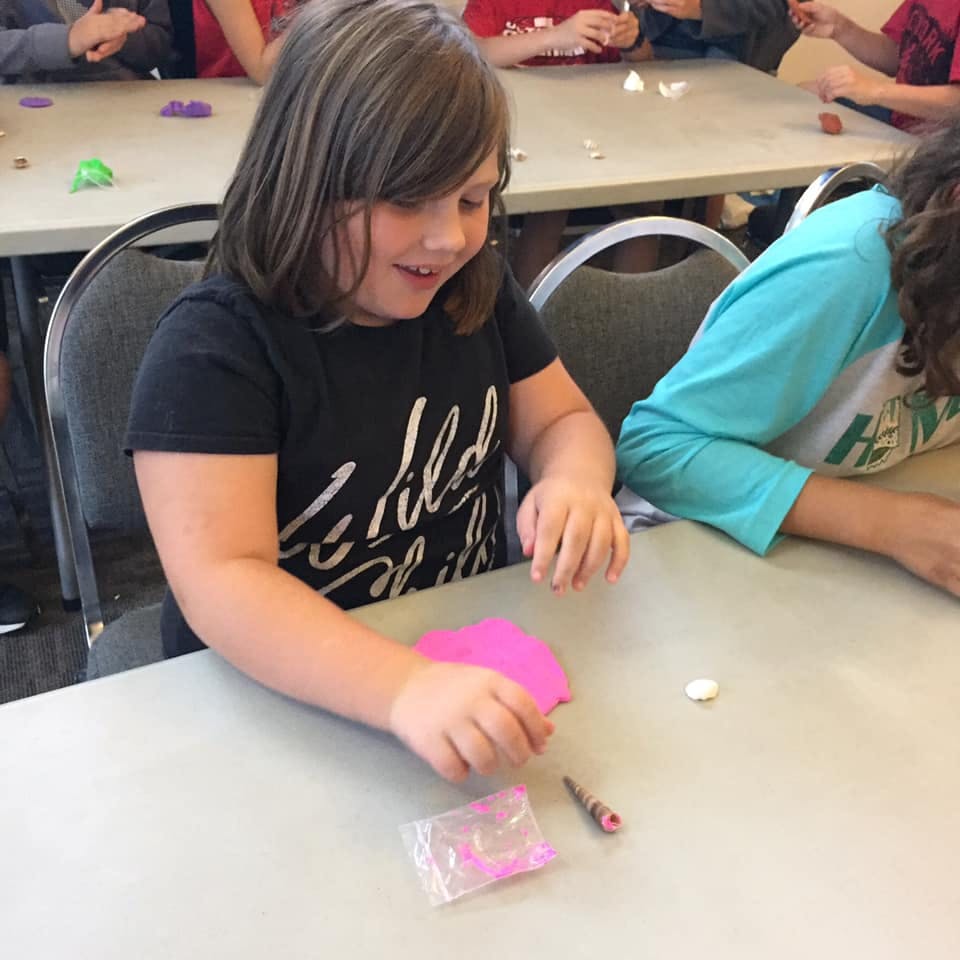 Child at a table holding pink modeling clay