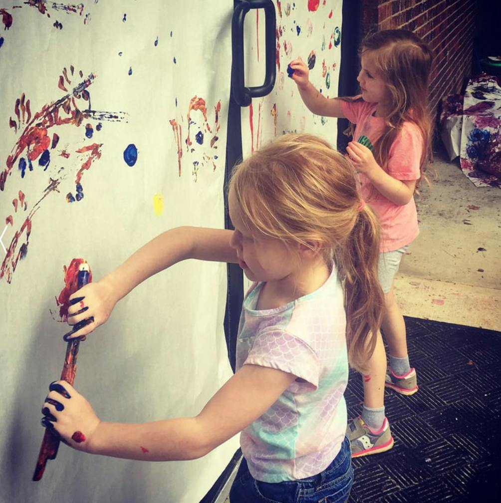 Two children painting on a large white surface