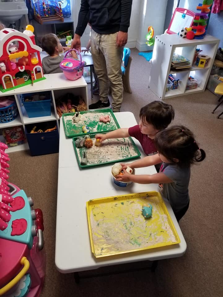 Two children playing with sensory bins at a table