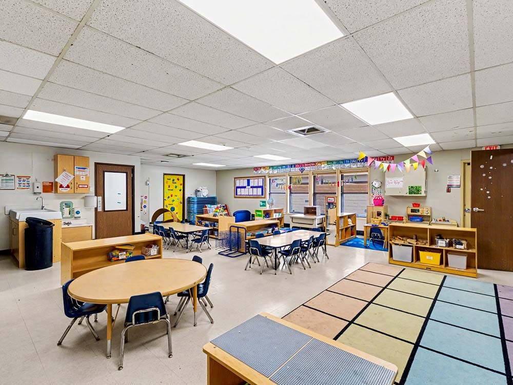 Empty classroom with small tables and chairs, a sink, and storage cubbies