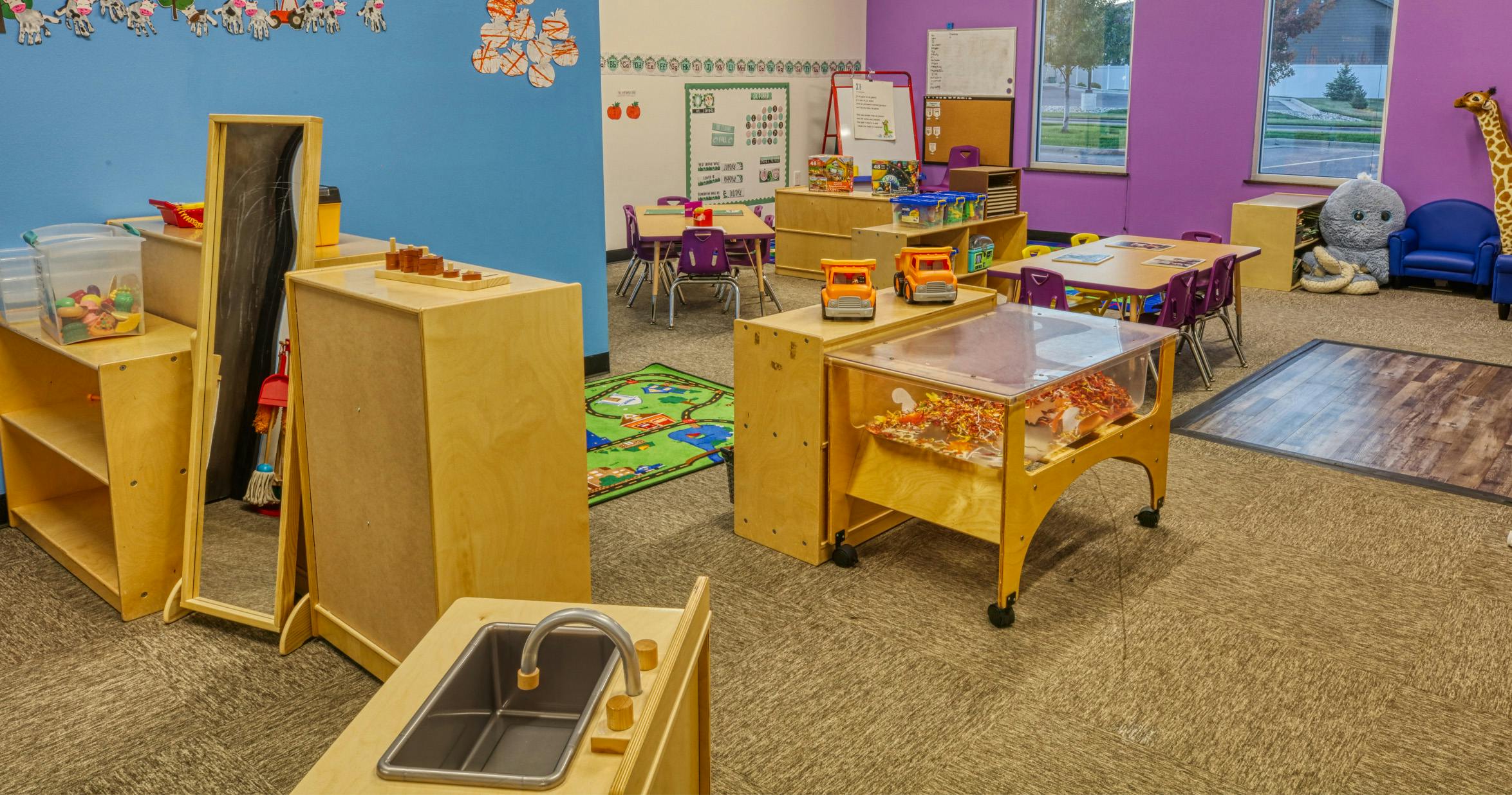 Children's classroom with blue and purple walls, play kitchen, sand and water table