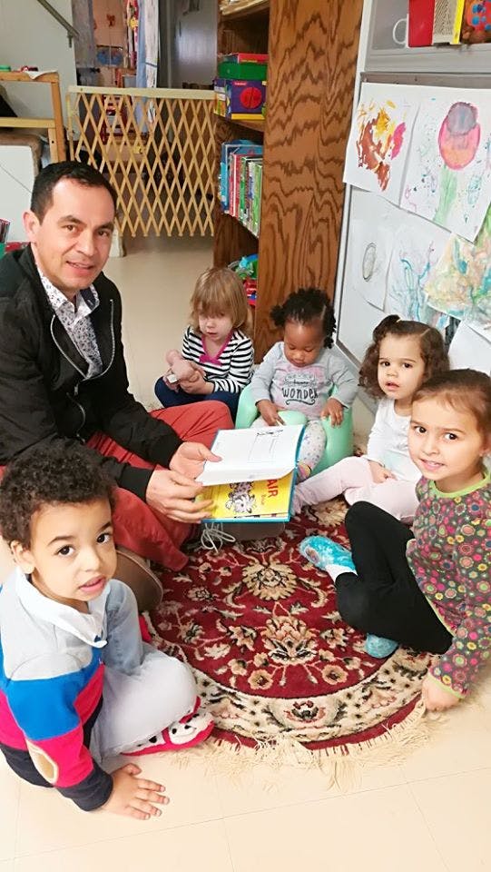 Adult reading a book to four children in a classroom