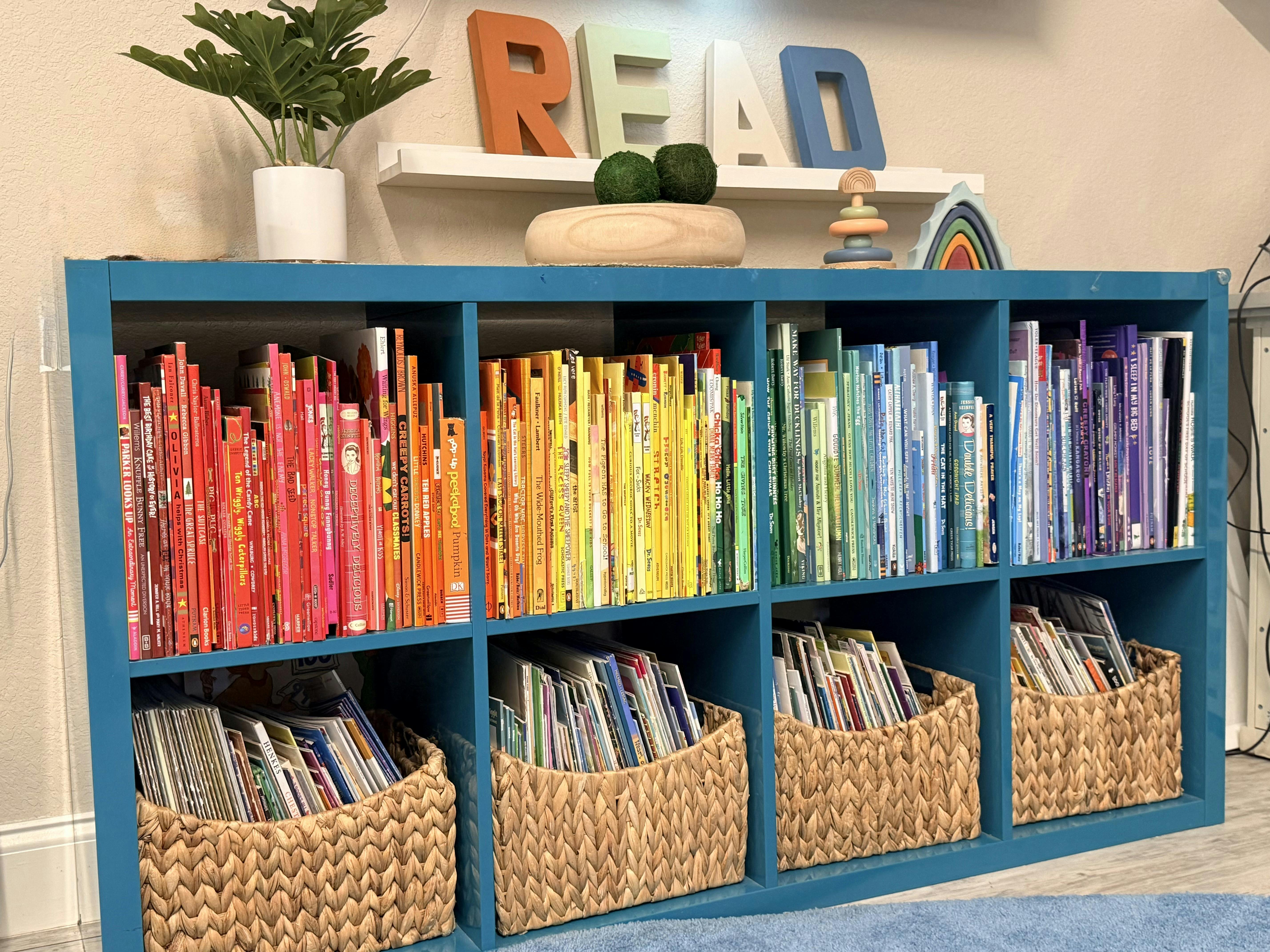 Bookshelves filled with children's books arranged by color, and wicker baskets below