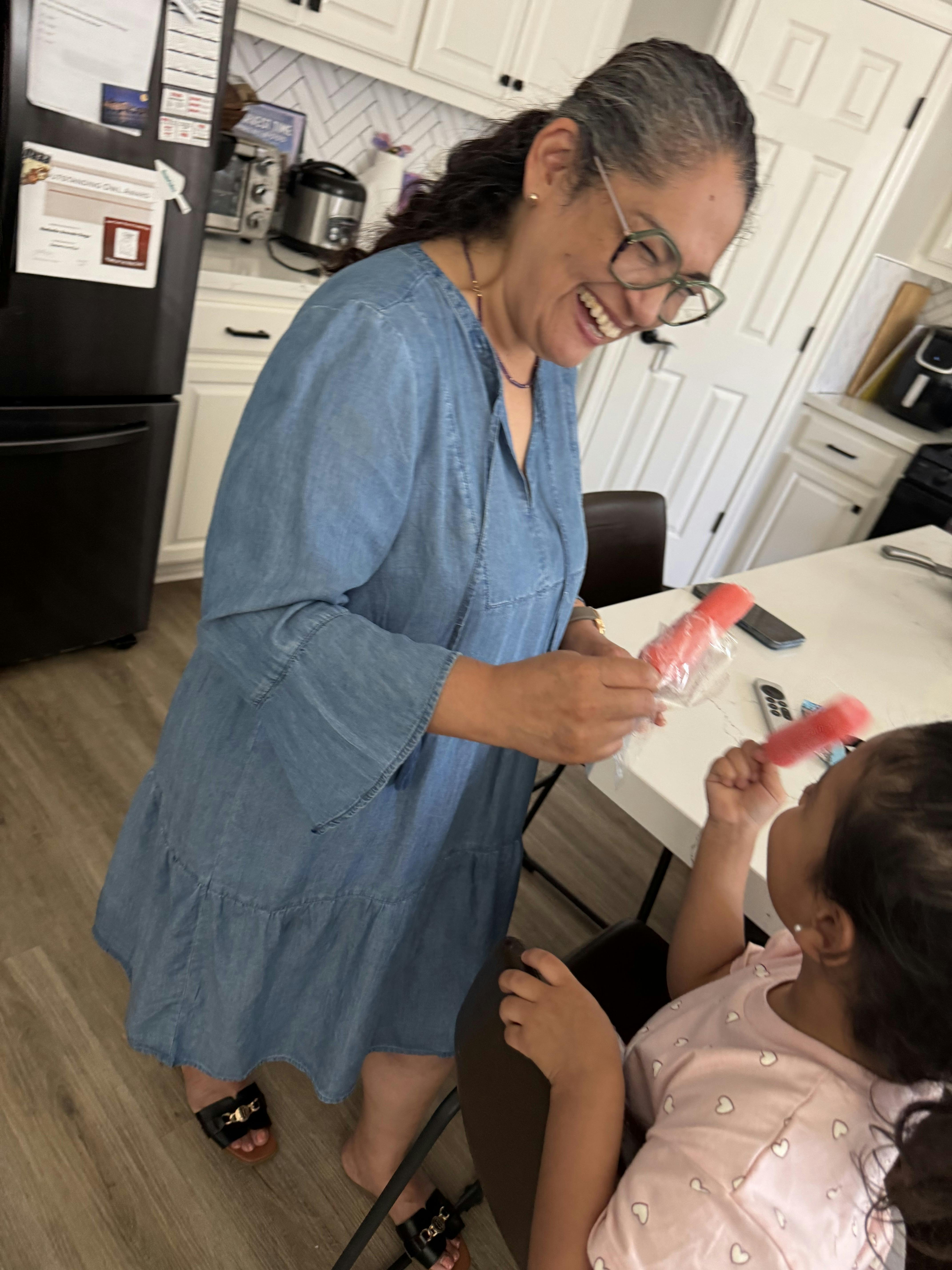 Laughing person giving a child a red ice pop in a kitchen