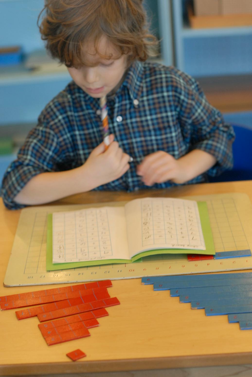Child writing in a notebook at a desk with math manipulatives