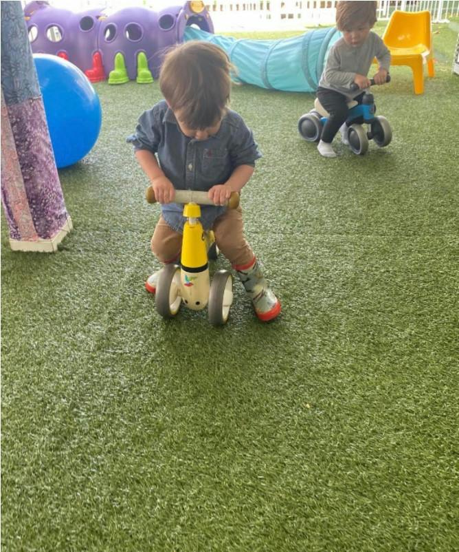 Two children riding balance bikes on artificial grass at a playground