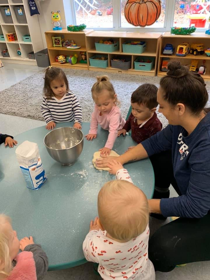 Adult and children kneading dough at a table in a classroom