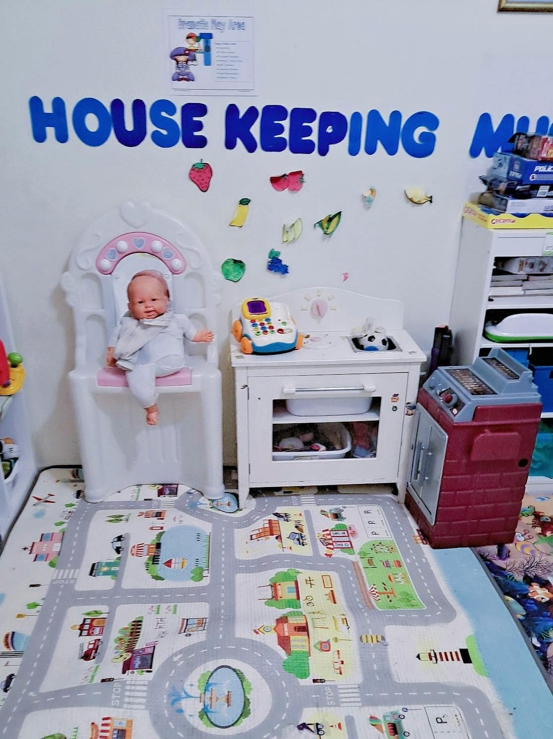 Child sitting in a high chair in a play area with toy kitchen and road map mat