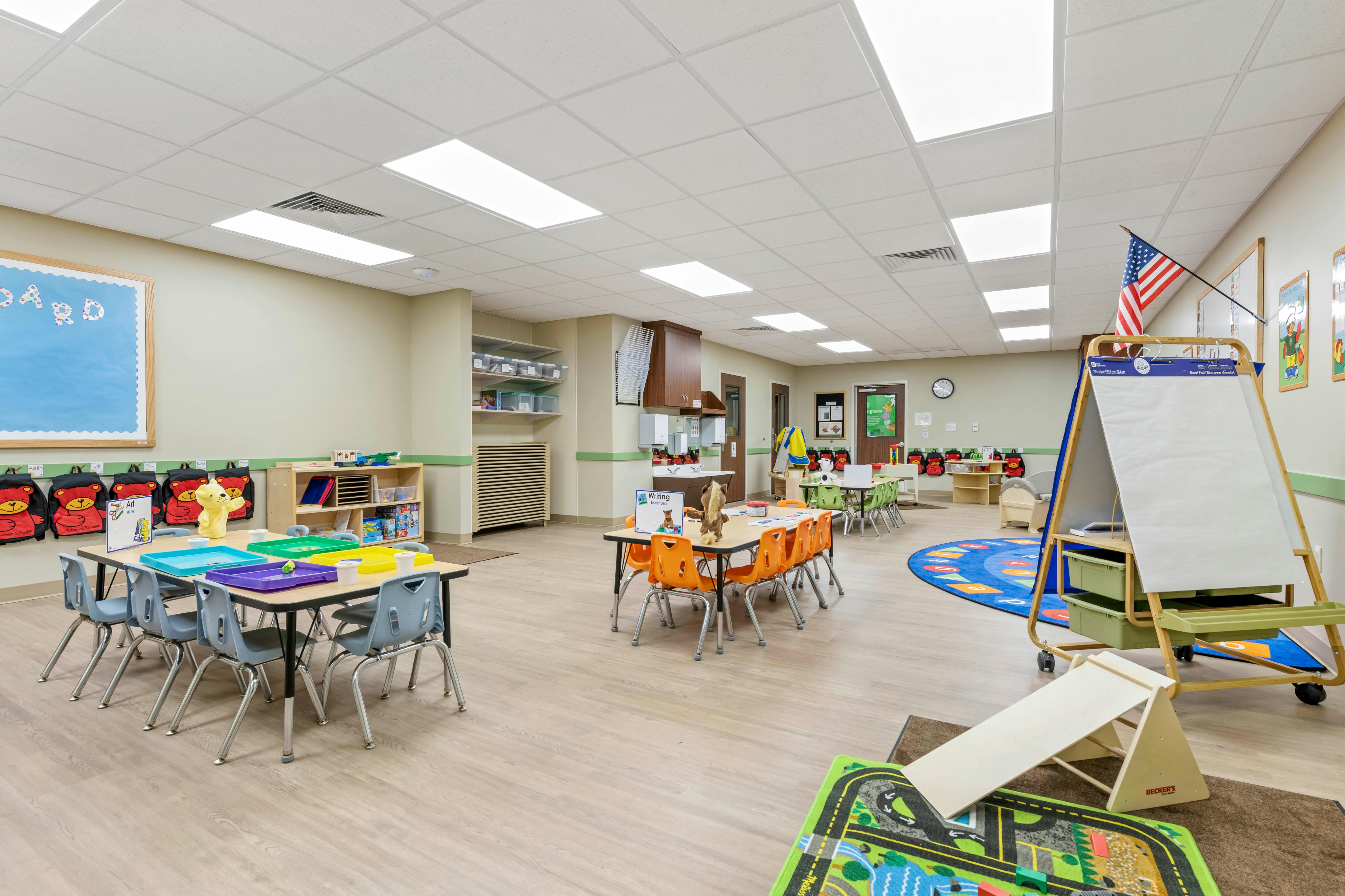 Classroom with child-sized tables and chairs, cubbies, an easel, and activity rug