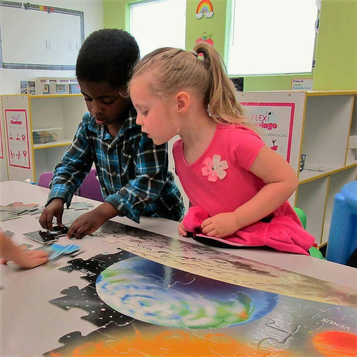 Two children assembling a large floor puzzle in a classroom