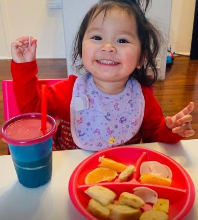 Child in a bib sitting at a table with a drink and a plate of food