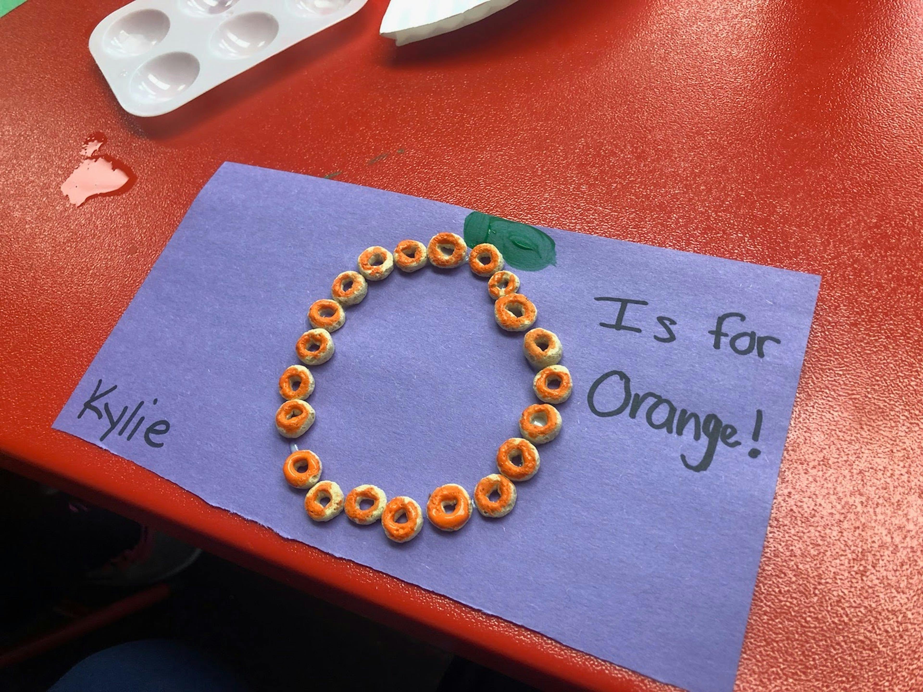 Cereal pieces arranged in a circle on purple paper with "I is for Orange!"