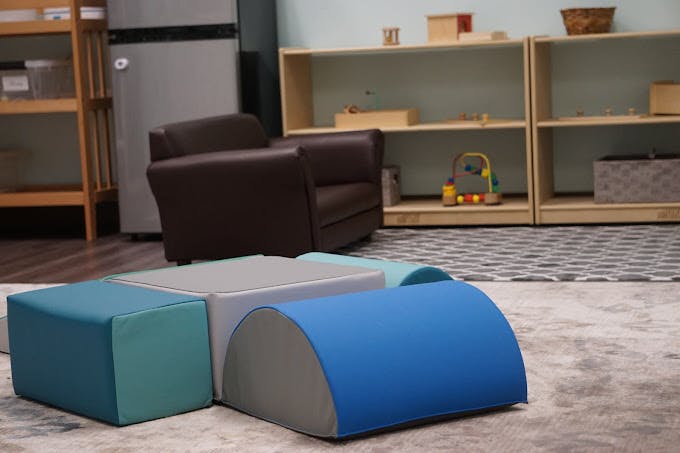 Soft play blocks on a rug in a room with shelves and a chair