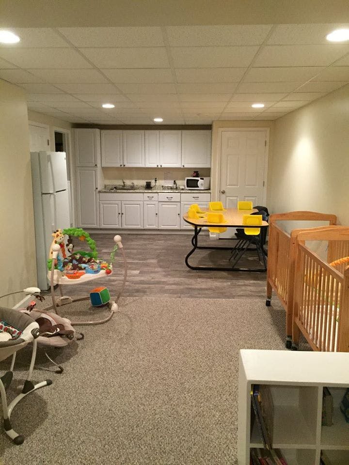 Room with kitchen, table and chairs, baby bouncer, and two cribs