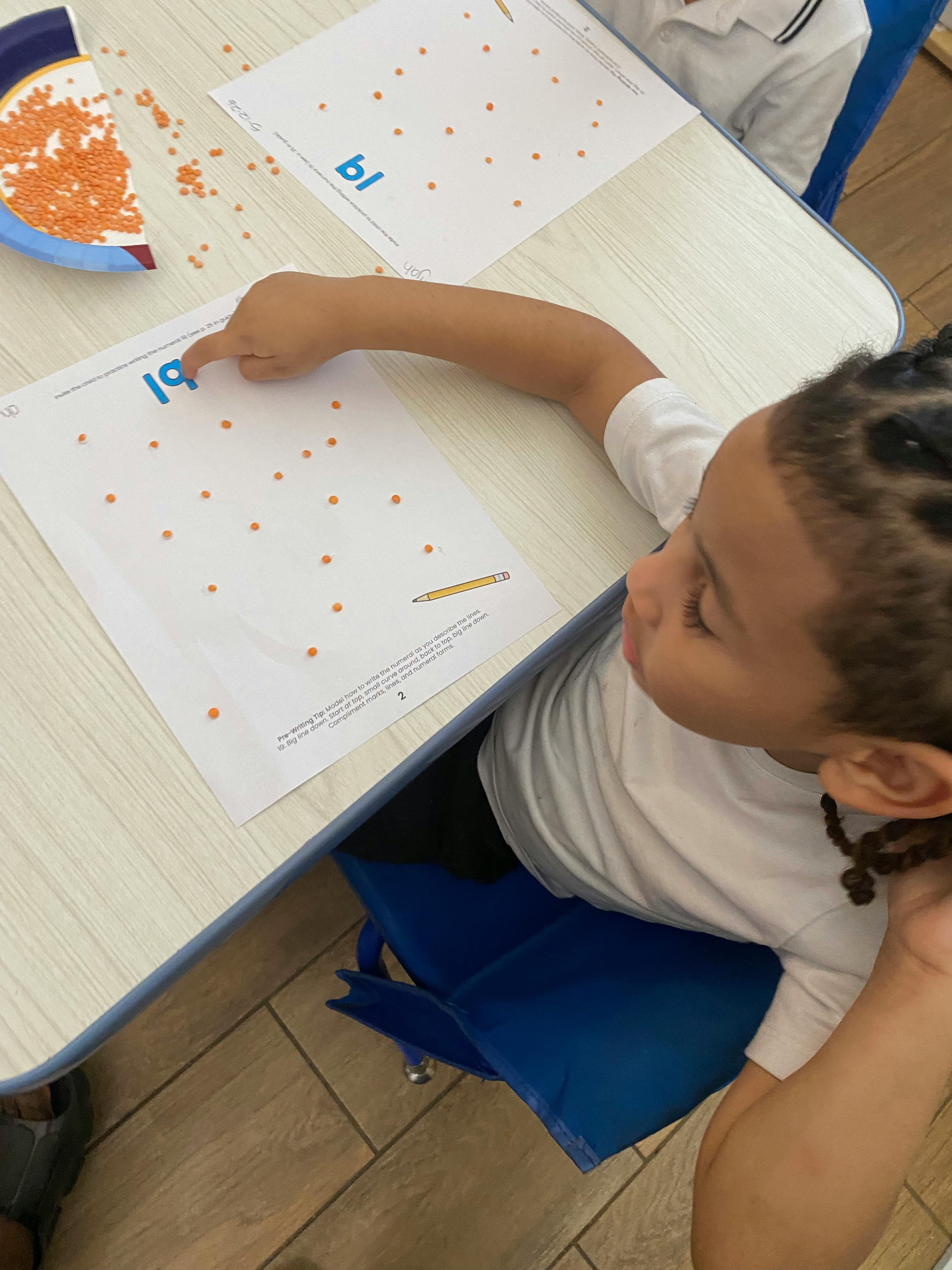 Child at a table pointing to the letters "bl" on a worksheet