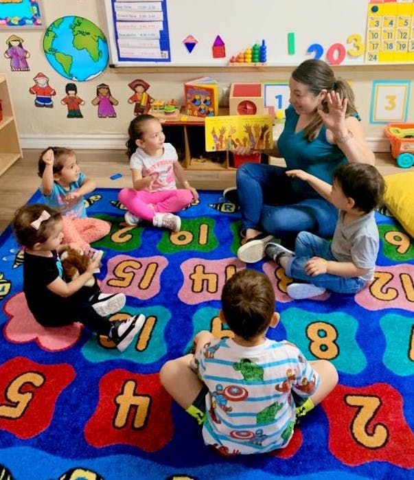 Adult and multiple children sitting on a number rug in a classroom