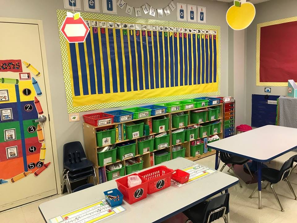 Classroom with tables, chairs, and storage shelves with green bins