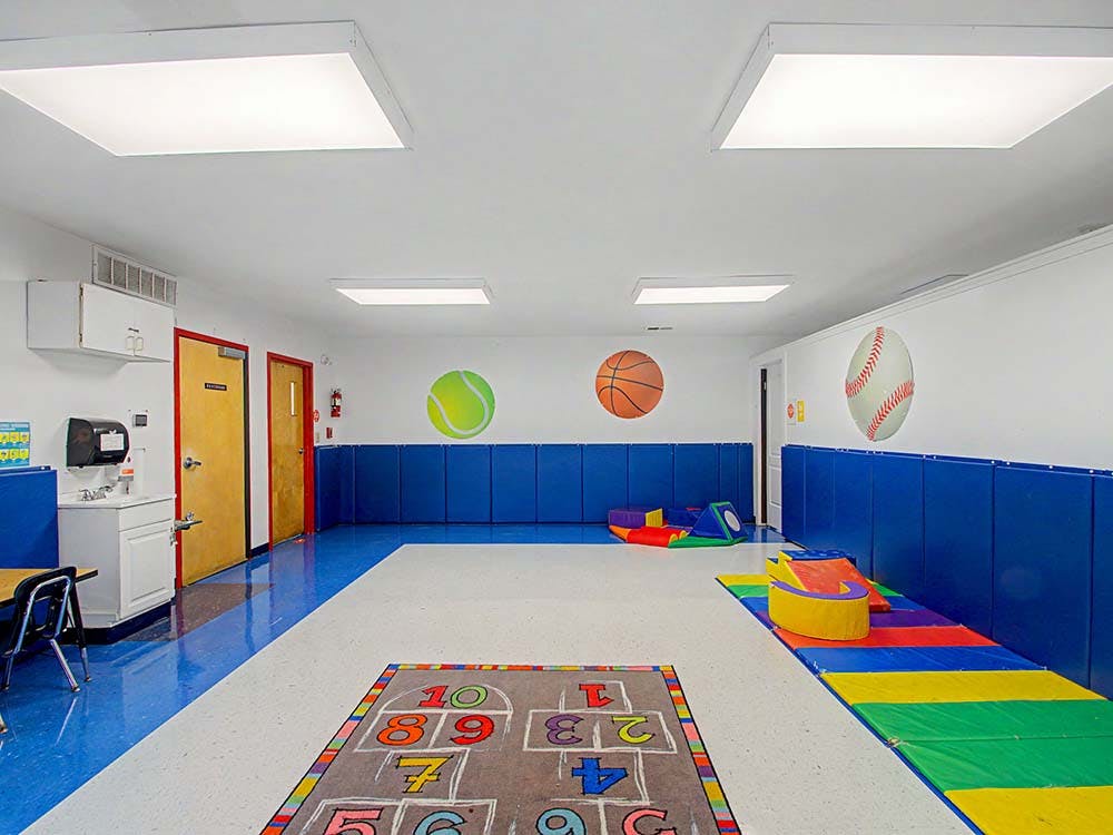 Empty children's playroom with blue and white flooring, hopscotch mat, and colorful soft play equipment