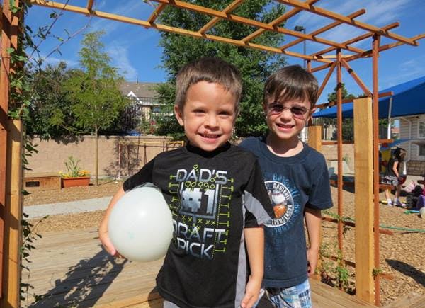Two children standing outdoors, one holding a white balloon