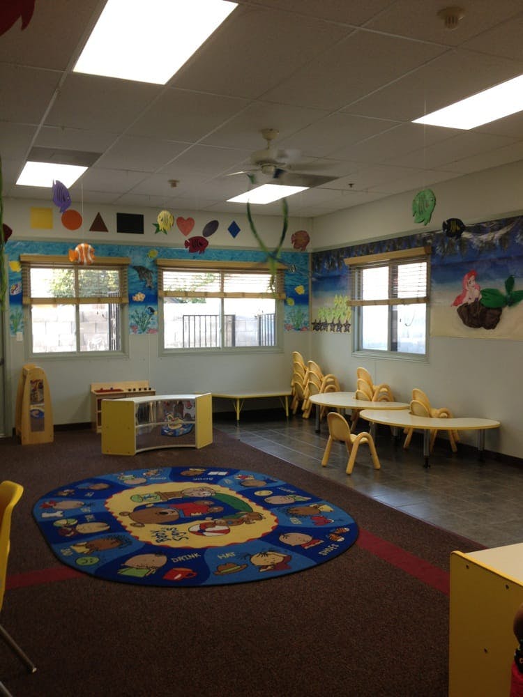 Empty classroom with small tables and chairs, a colorful rug, and decorated walls