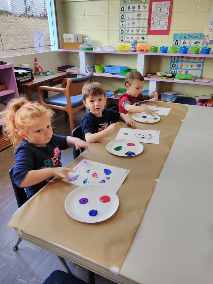 Three children painting at a table in a classroom