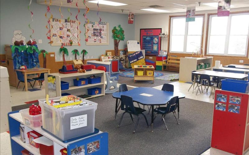 A colorful empty classroom with small tables, chairs, and learning materials