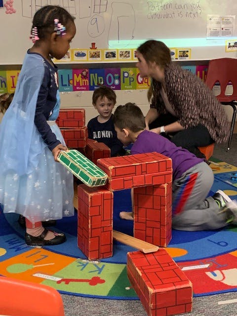 Adult and children playing with building blocks in a classroom