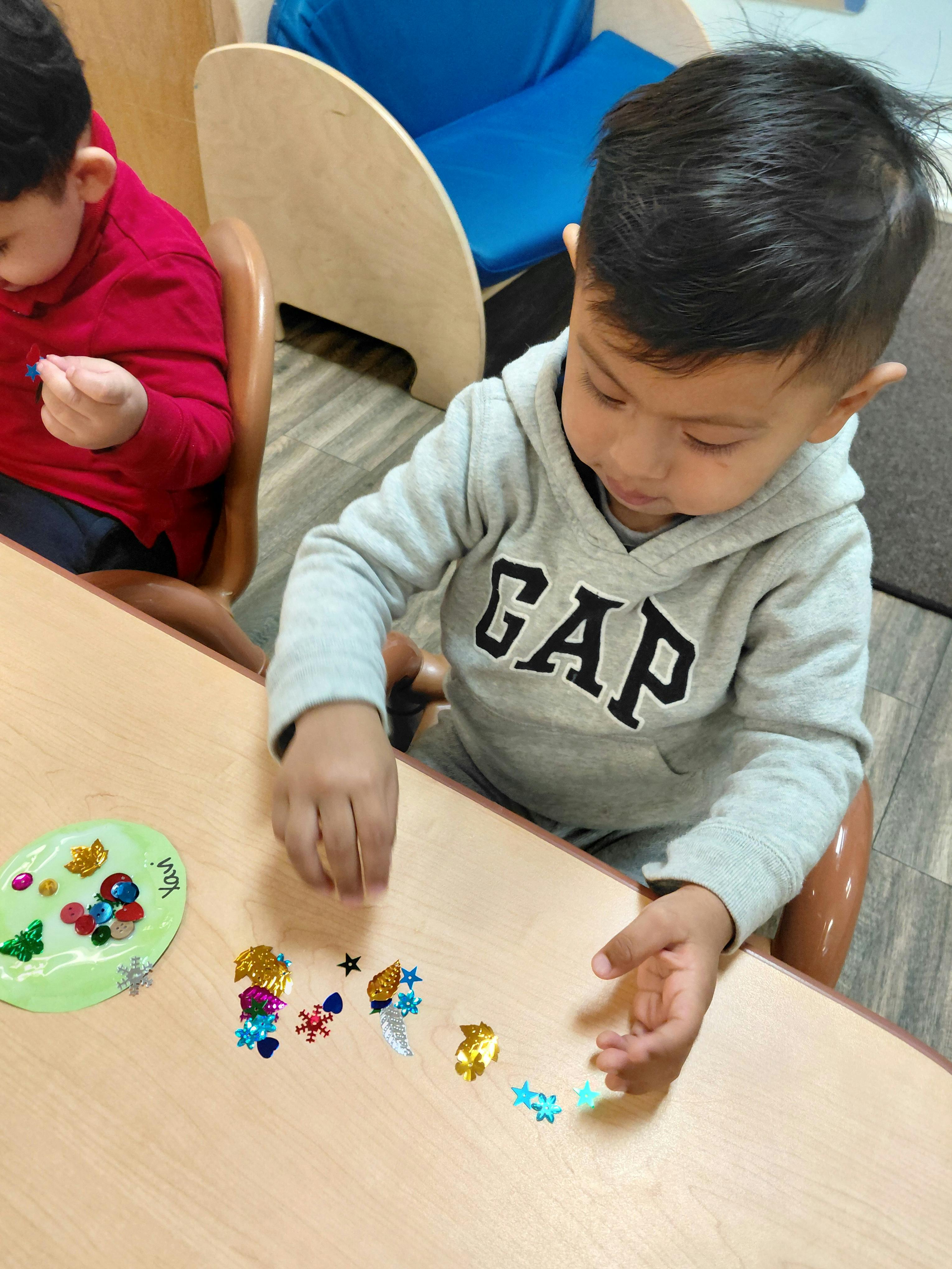 Child in a gray hoodie playing with colorful sequins on a table