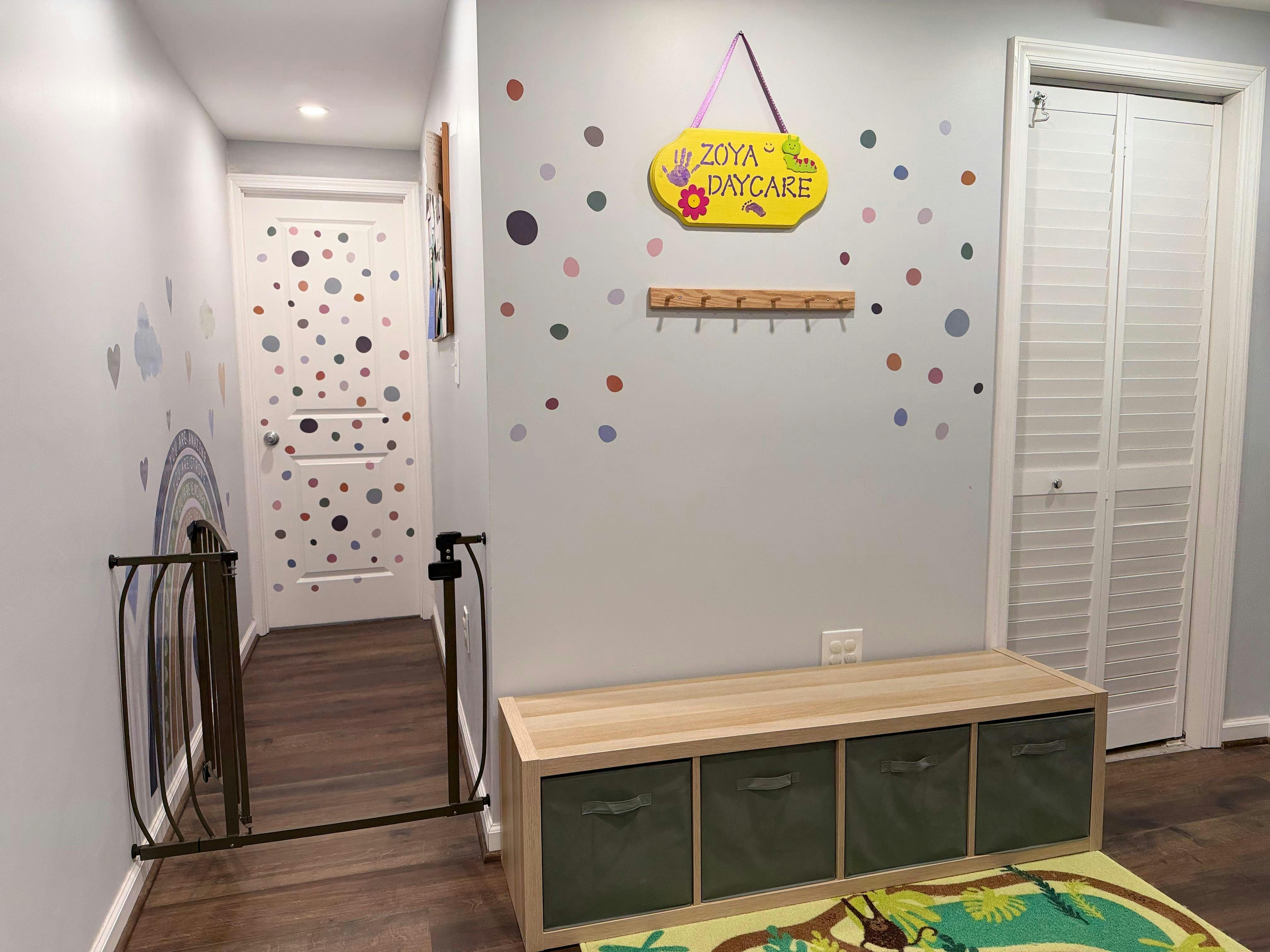 Hallway with a baby gate, a colorful polka dot wall, and a yellow "Zoya Daycare" sign