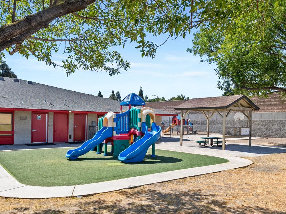 Playground with slides and climbing structure on artificial turf with a building in background
