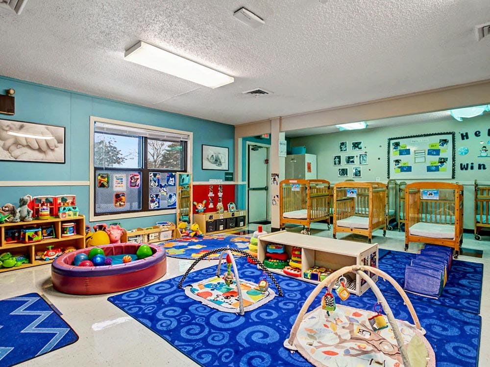 A colorful childcare room with cribs, play mats, and toys