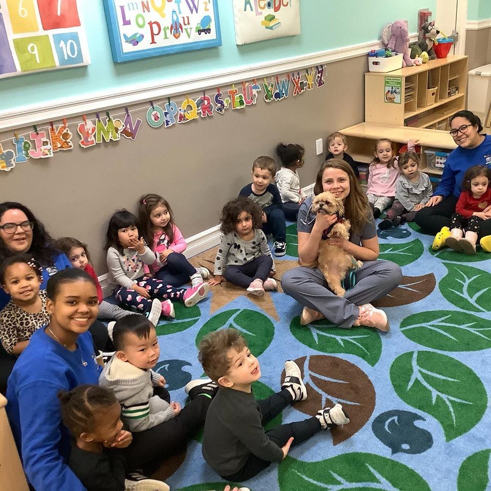 Adults and children sitting on a rug with a person holding a small dog
