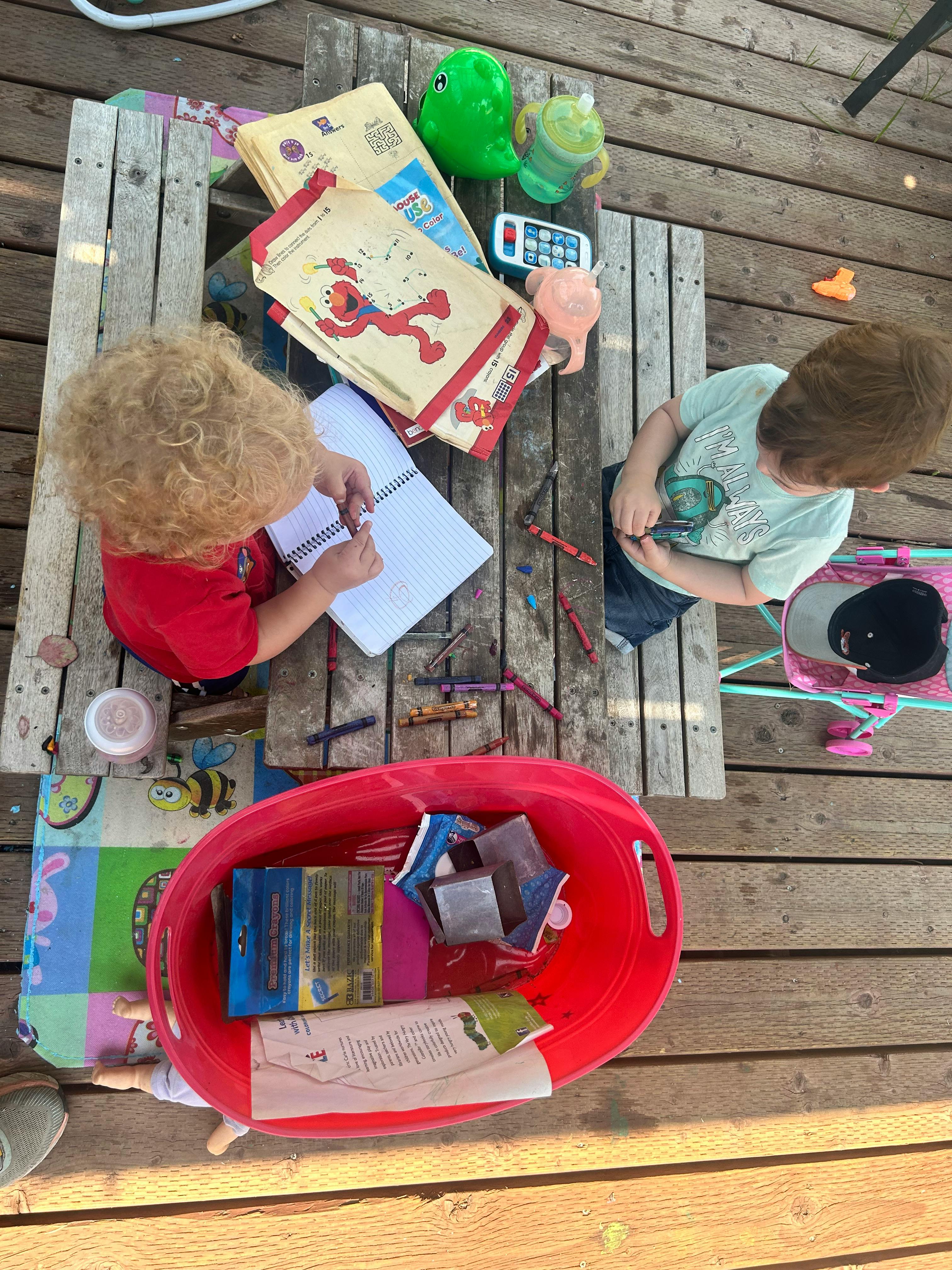 Two children playing with toys and drawing at a wooden table