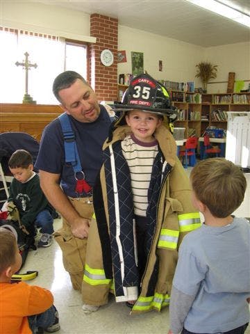 Adult helping a child try on a firefighter's helmet and jacket