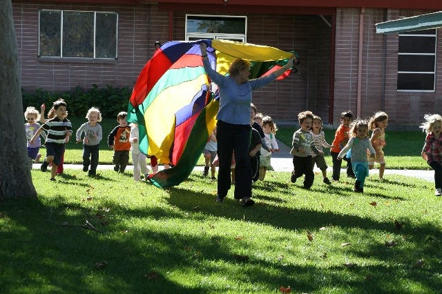 Person holding a colorful parachute with children running around on grass