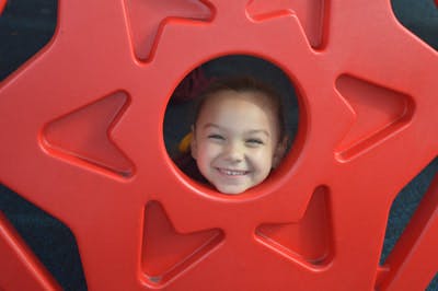 Child's face peeking through a red playground structure