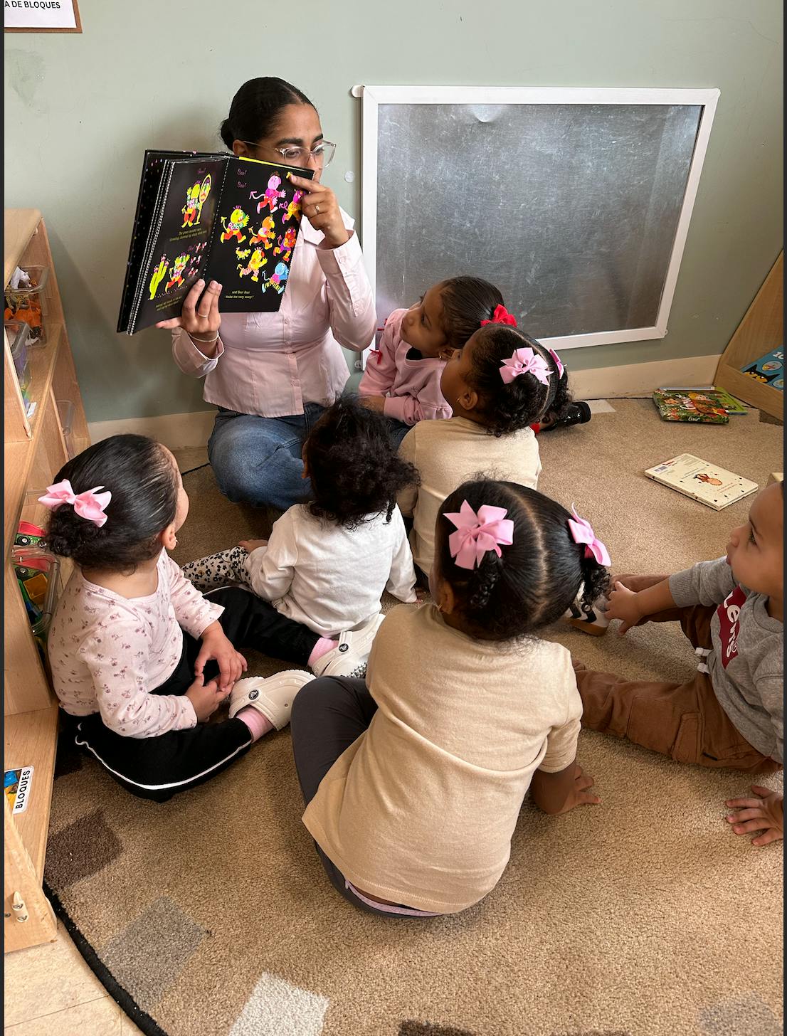 Adult reading a book aloud to a group of children seated on a classroom rug