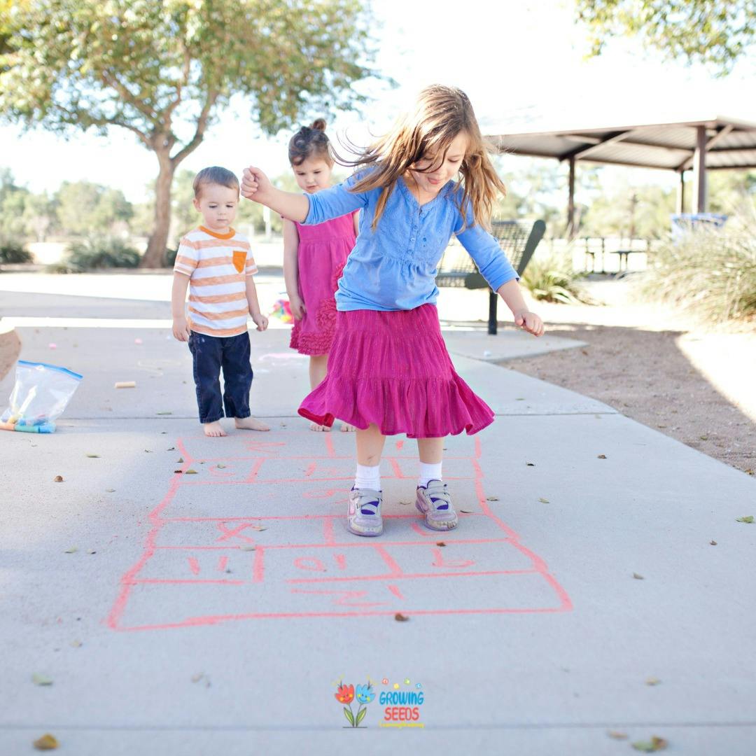 Child playing hopscotch with two other children nearby