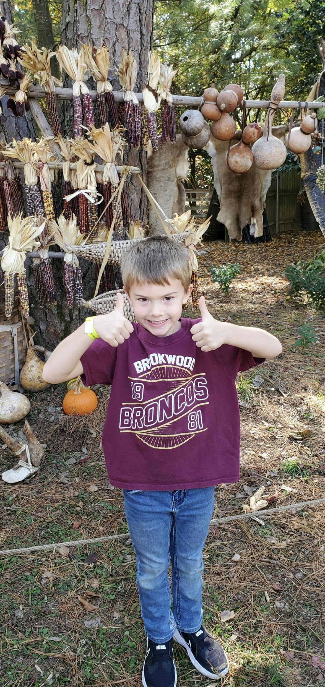 Child giving two thumbs up in front of decorative corn and gourds