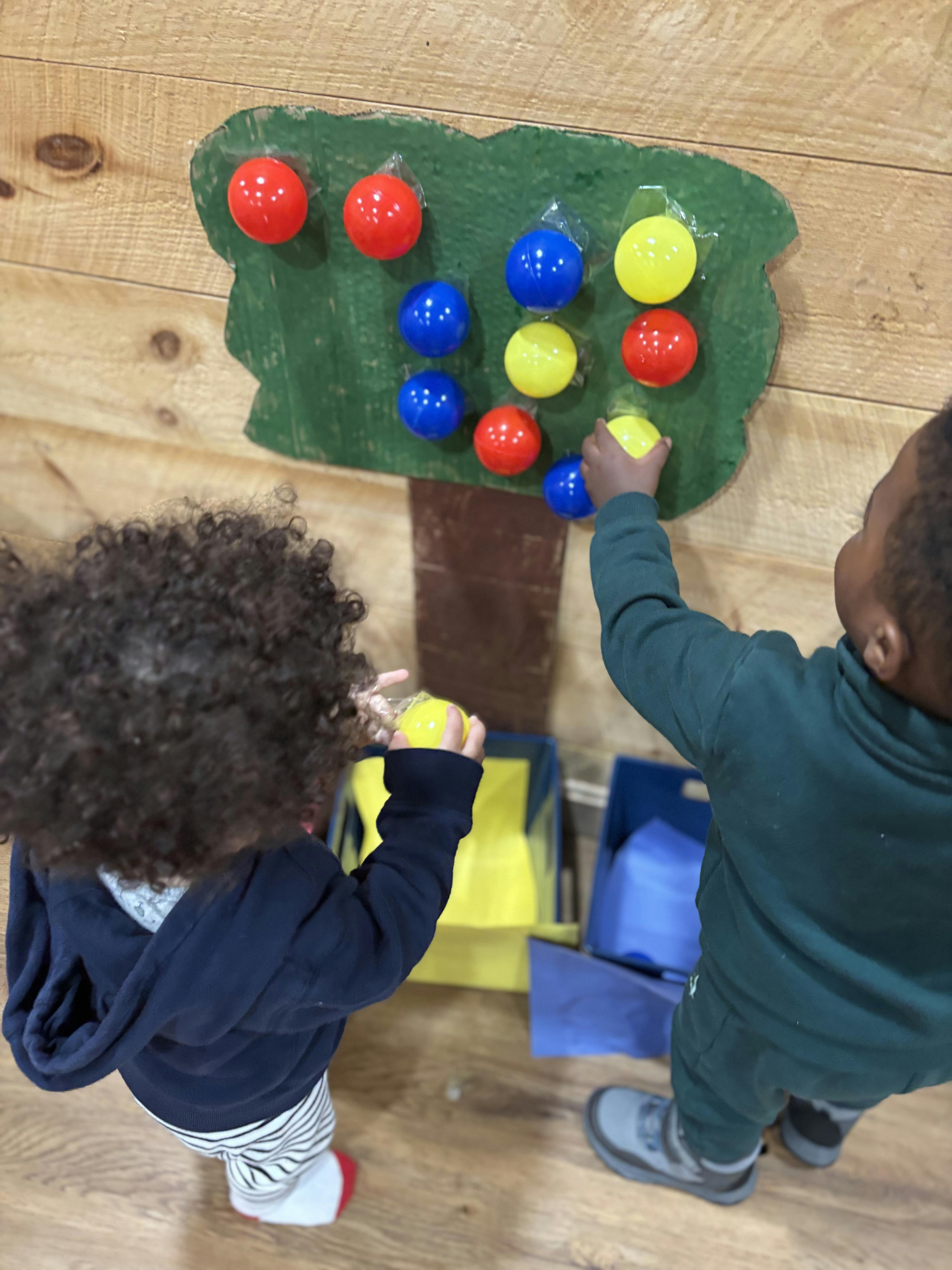 Two children playing with a ball sorting activity on a wooden wall
