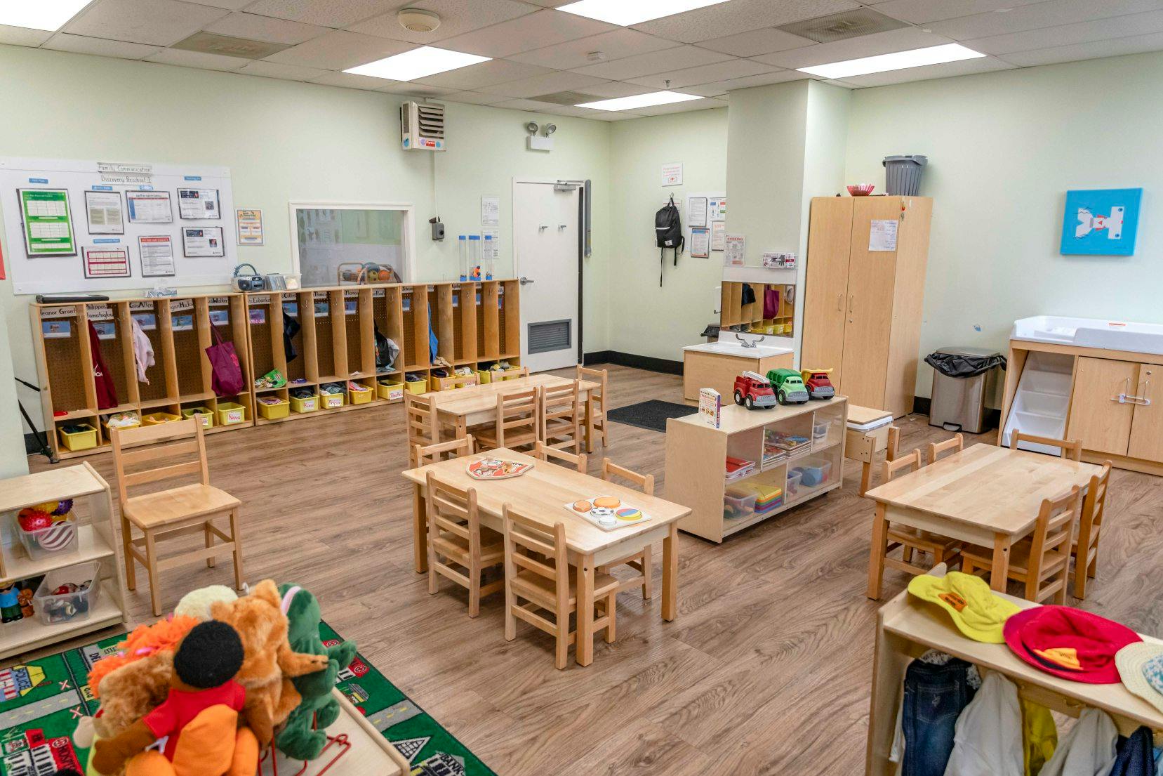 An empty classroom with small wooden tables and chairs, cubbies, and various learning materials