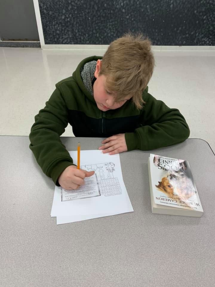 Child writing on paper at a desk with a book nearby