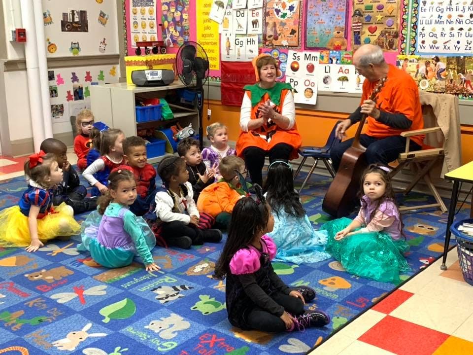 Adults playing guitar and reading to children in a classroom