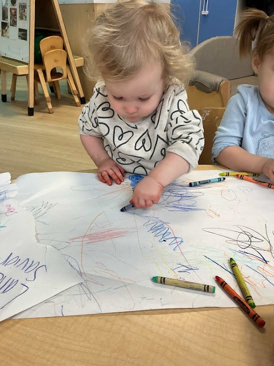 Child coloring on a large sheet of paper with crayons