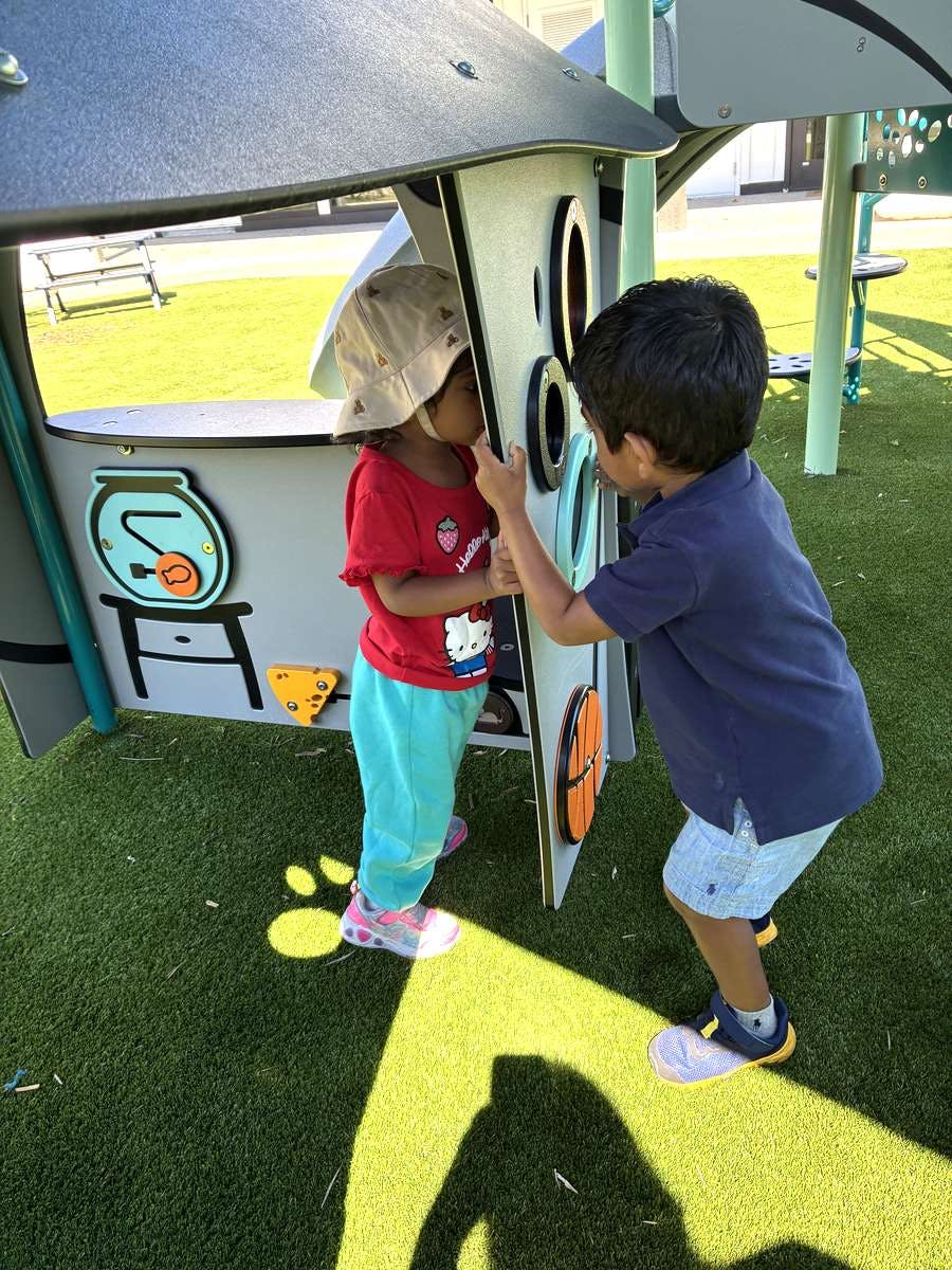 Two children playing with sensory panels on a playground structure